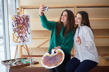 Beautiful young designers are making selfie using a smart phone and smiling while working in studio