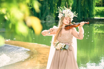 girl in a dress plays the violin near a waterfall.