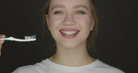 Happy young woman brushing teeth with activated charcoal tooth paste on dark background - Powered by Adobe