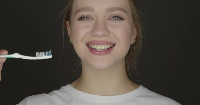 Happy young woman brushing teeth with activated charcoal tooth paste on dark background
