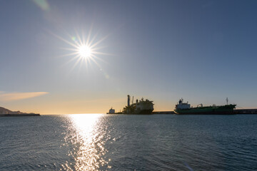 Obraz premium Large ships moored in the harbor in Motril with the sun shining in the sky reflecting on the water, Andalucia Spain.