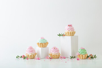 pink and green cupcakes with spring flowers  on wooden podiums on white  background