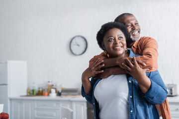 happy and senior african american man embracing smiling wife.