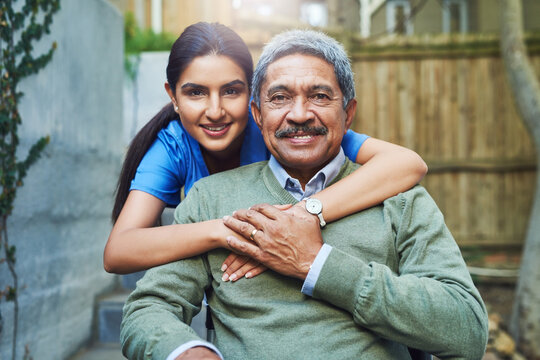 She Has Helped Me Some Difficult Times. Portrait Of A Cheerful Young Female Nurse Holding A Elderly Patient In A Wheelchair As Support Outside During The Day.