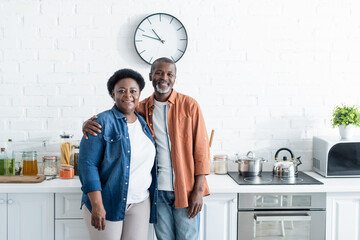 happy senior african american couple looking at camera in kitchen.