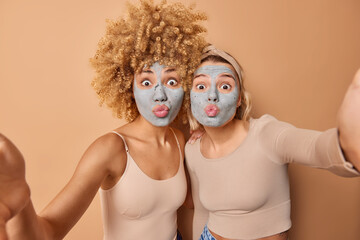 Lovely young women make grimace at camera keep lips folded apply beauty clay mask to reduce fine lines dressed casually isolated over brown background. Facial treatments and skin care concept