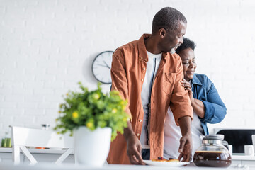 happy senior african american woman hugging husband near breakfast in kitchen. - Powered by Adobe