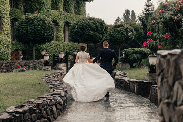 the bride and groom in a lush white dress running in the rain against the backdrop of a beautiful building overgrown with ivy