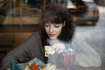 Young woman eating and using phone while sitting in cafe.