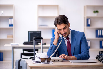 Young male employee preparing for trip at workplace