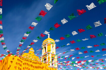 Yellow Catholic Church and holiday flags against a blue sky. Mexico. Old city of Izamal.