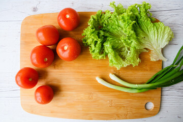 Fresh vegetables for salad lie on a wooden table with a cutting board. Top view. Close-up.