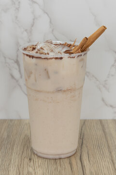 Sweet horchata beverage is featured in a clear plastic cup garnished with spice on the rim and cinnamon sticks