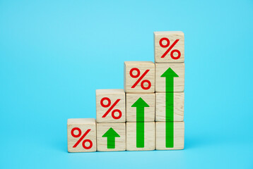 Interest rate financial and mortgage rates concept. Wooden cube block increasing on top with icon percentage symbol and arrow upward direction on a blue background.                         