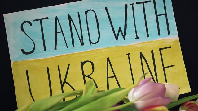 Inscription Stand with Ukraine on motivational packard against armored conflict on background of yellow blue flag with flowers. Crisis, peace, stop aggression in whole world