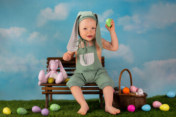 small child dressed as an easter bunny sits on a bench with colored eggs - 499684940