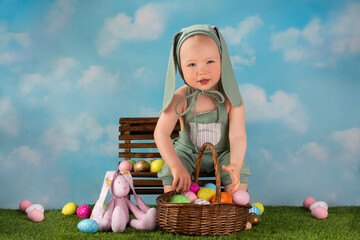 small child dressed as an easter bunny sits on a bench with colored eggs - 499684941