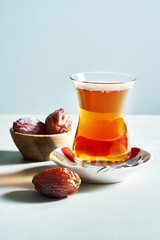 Traditional Turkish black tea in glass on saucer with dates on white background with copy space.