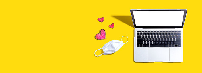 Laptop computer with a facial mask and hearts - overhead view