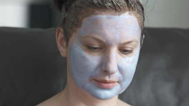 Woman with facial cosmetic mask applied on her face dyes her hair at home, female face close-up. High quality 4k footage