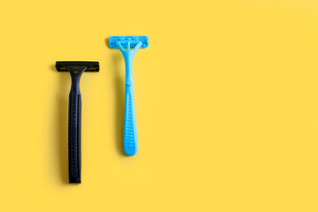 Two plastic razors in black and blue on a yellow background. Male and female disposable razor with free space for text. The concept of care for appearance and care for smooth skin