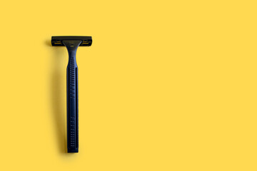 Disposable plastic razor on a yellow isolated background. Black men's razor with free space for text on a yellow background. Skin care razor and neat look concept