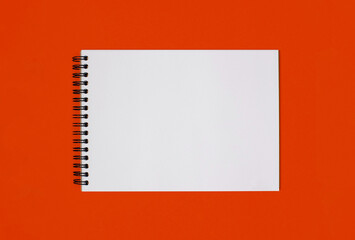 Notebook made of white paper with binding on a orange background. Empty notepad without notes with free space for text. Notebook in a classic binding without marks on a horizontal photo