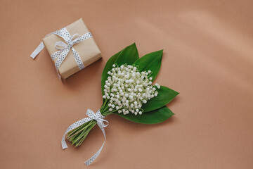 Bouquet of Lily of the valley flowers and gift on beige background.