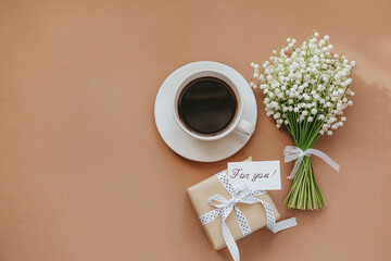 Bouquet of Lily of the valley flowers, gift and cup of coffee on beige background.