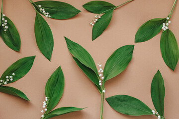 Lily of the valley flowers with green leavesn beige background. Flower pattern. . Flat lay.