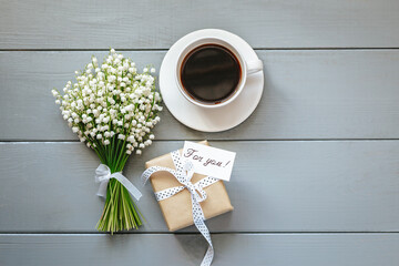 Bouquet of Lily of the valley flowers, gift and cup of coffee on grey wooden background.