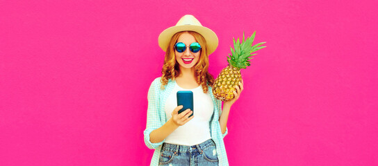 Summer portrait of happy smiling woman with smartphone and pineapple wearing straw hat, sunglasses on pink background