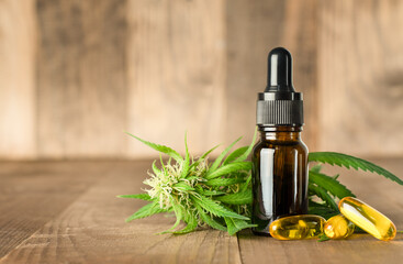 CBD oil, cannabis plant and capsules on wooden background