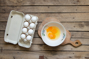 Eggs in a tray and a broken egg in a plate on a wooden table ,cooking an omelette