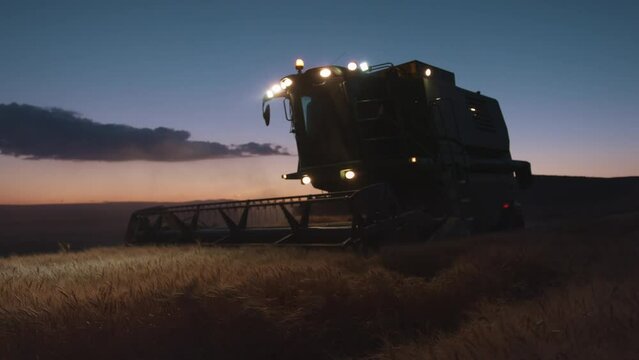 A combine harvester is working on a wheat field right before sunset in slow motion.