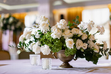 Large white bouquets of roses stand on dinner tables decorated with golden glasses 