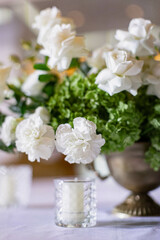Large white bouquets of roses stand on dinner tables decorated with golden glasses 