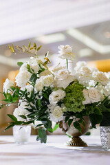 Large white bouquets of roses stand on dinner tables decorated with golden glasses 