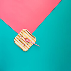 Gold and white striped paper plate with three rubber ice creams and pink plastic spoon on pink and blue background. Minimal concept.
