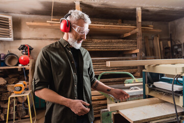 grey haired carpenter working near thickness planer in workshop.