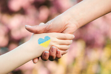 Obraz na płótnie Canvas Support for Ukrainian children. Ukrainian child holds a volunteer's hand.