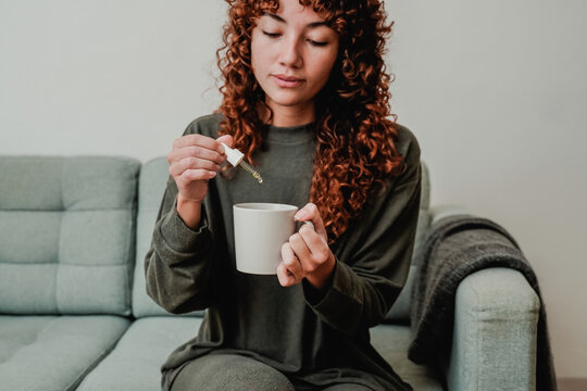 Cbd hemp oil - Woman taking cannabis oil in tea cup - Focus on hand holding dropper