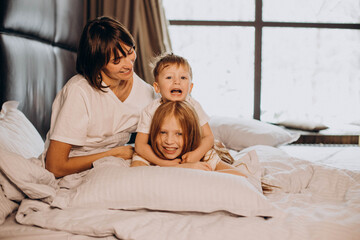 Fototapeta premium Mother with son and daughter having fun in bed