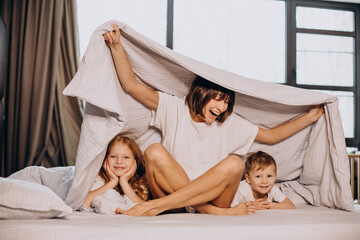 Mother with son and daughter sitting on bed under the blanket