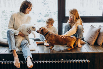 Mother with son and daughter playing with their dog at home by the window