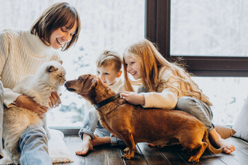 Mother with son and daughter playing with their dog at home by the window