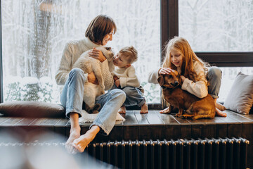 Mother with son and daughter playing with their dog at home by the window
