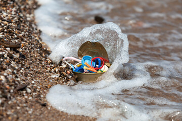 Naklejka premium Tin can with plastic garbage in wave. Concept - Environment. Household garbage and plastic waste of human activity in the sea. Selective focus