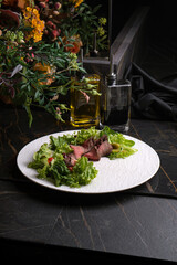 Salad with roast beef on a white dish on a black marble table
