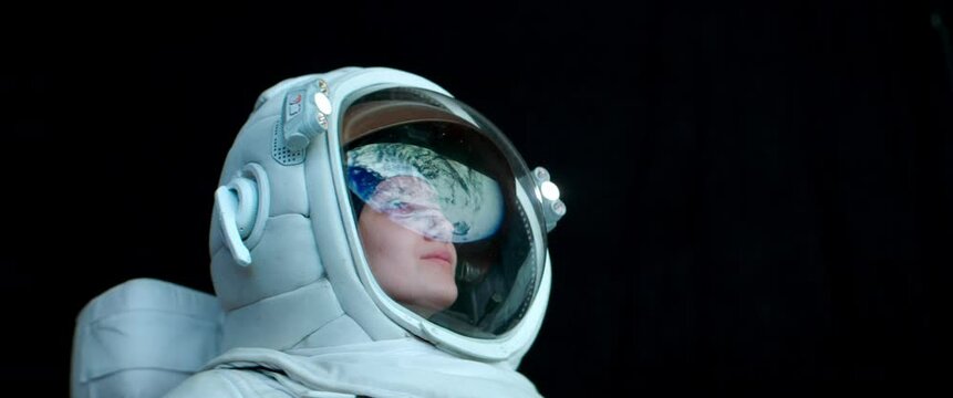 CU Portrait of Caucasian female astronaut during spacewalk. Earth reflecting in helmet visor. Space exploration concept. Shot with 2x anamorphic lens